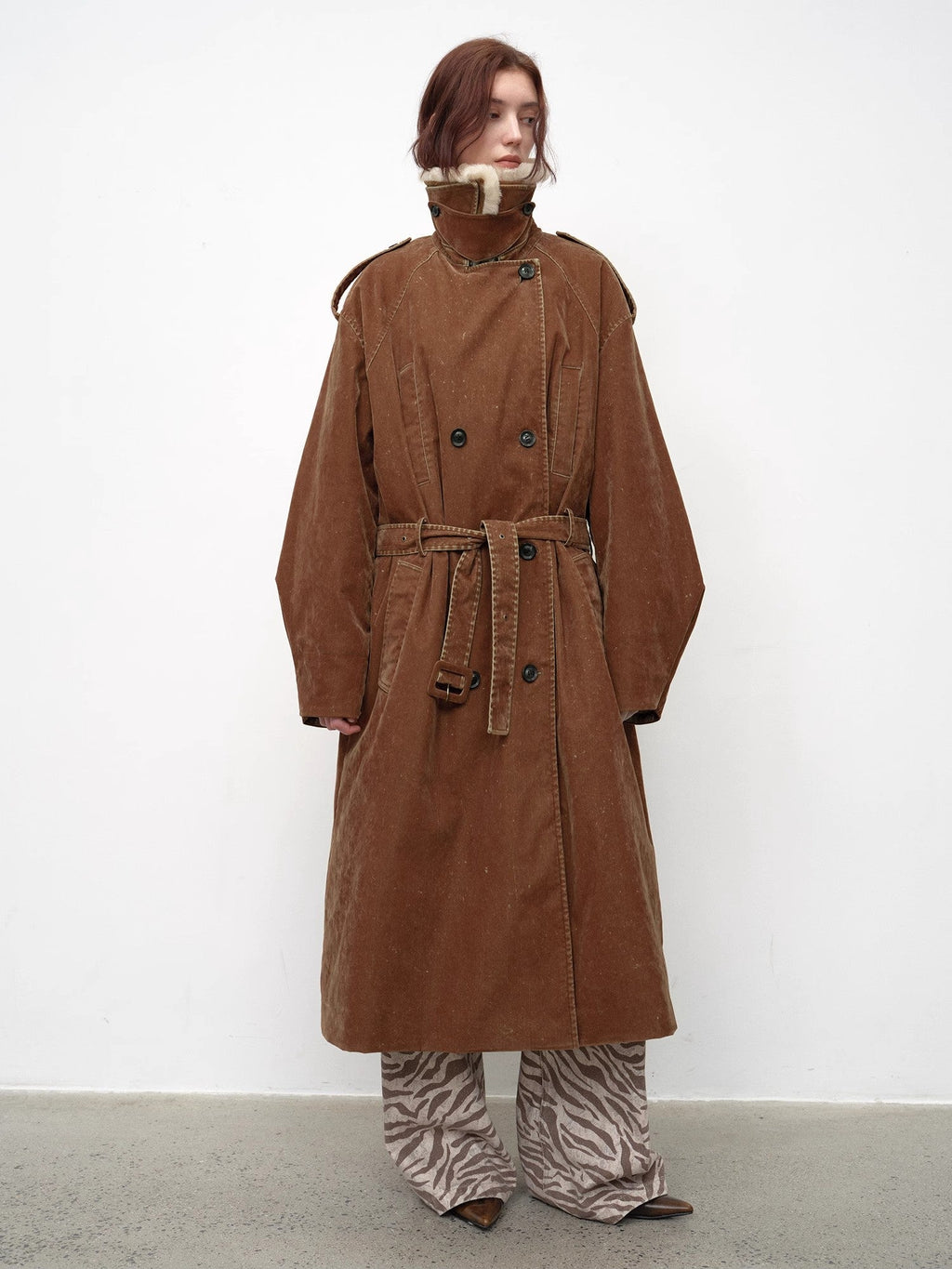 Person wearing a long brown coat with a white background