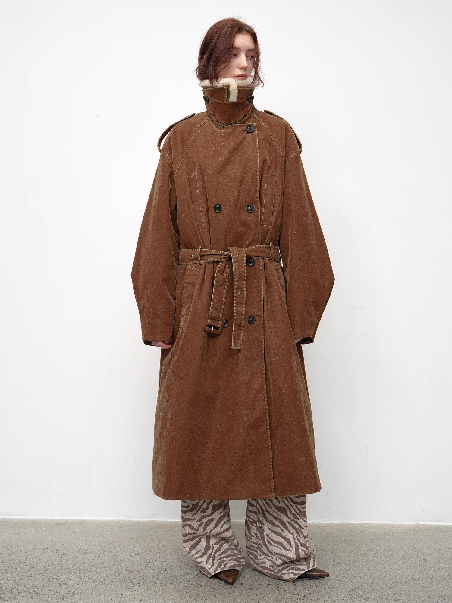 Person wearing a long brown coat with a white background