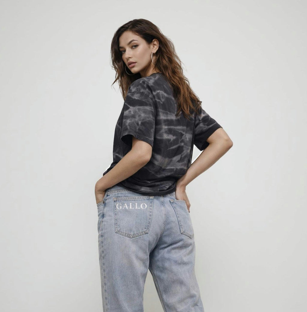 Woman wearing a tie-dye shirt and light blue jeans with 'GALLO' branding on a white background
