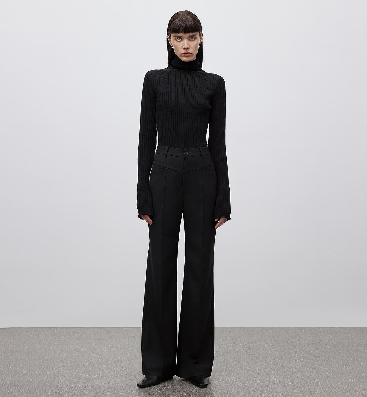 Person wearing a black turtleneck and wide-leg pants against a plain background